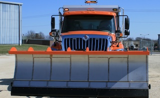 orange snow truck with a gray and orange plow sitting on concrete on a sunny day